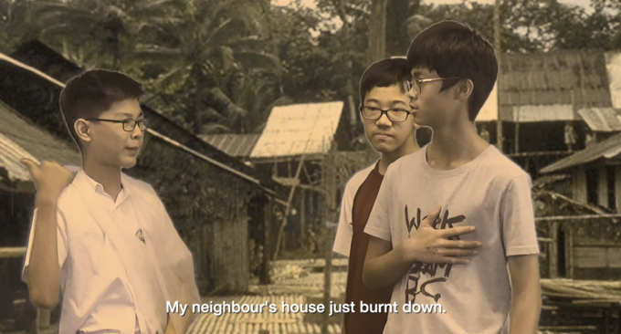 Three boys talking outdoors near rural buildings, with subtitle reading "My neighbour's house just burnt down."